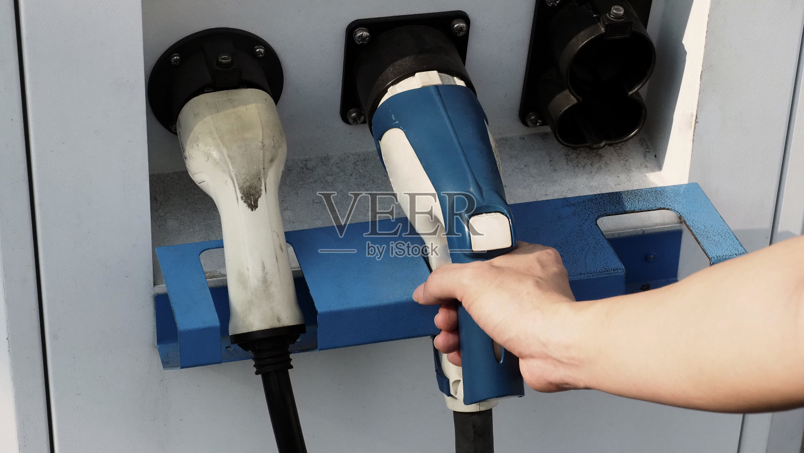 电动车司机手持电池充电器插头。手持电动汽车充电插头在相机前，室外背景模糊。可持续能源充电站背景照片摄影图片