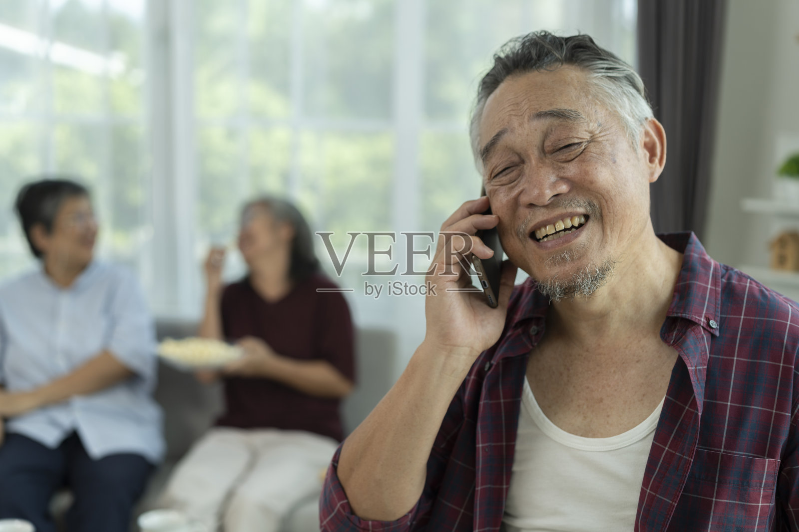 亚洲老年男子一边用手机，一边和两个女性朋友有说有笑照片摄影图片