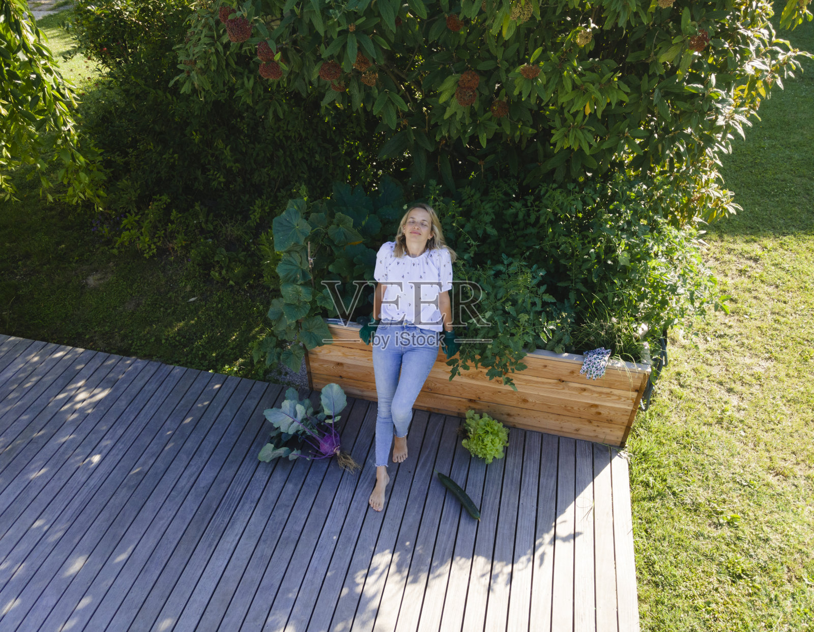 一个女人坐在一个有收获蔬菜的凸起的床前，很自豪照片摄影图片