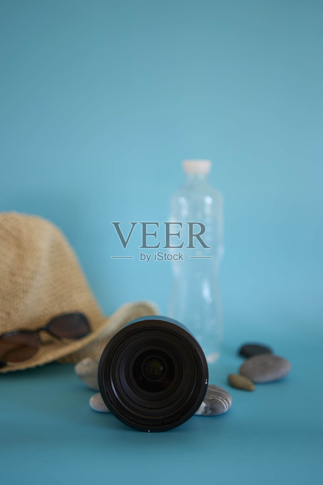 镜片，草帽，太阳镜，一瓶水，防晒喷雾，彩色背景上的鹅卵石照片摄影图片