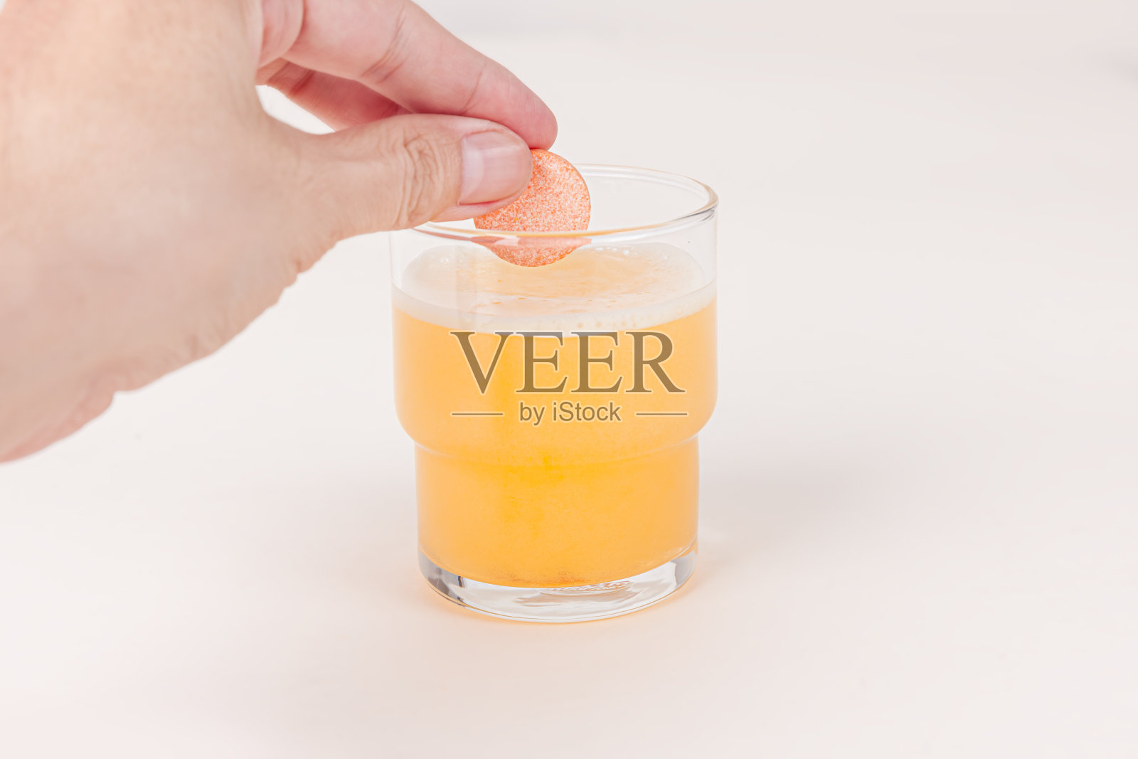 用手将橙色维生素C泡泡片滴入玻璃杯中，白色背景上有气泡照片摄影图片