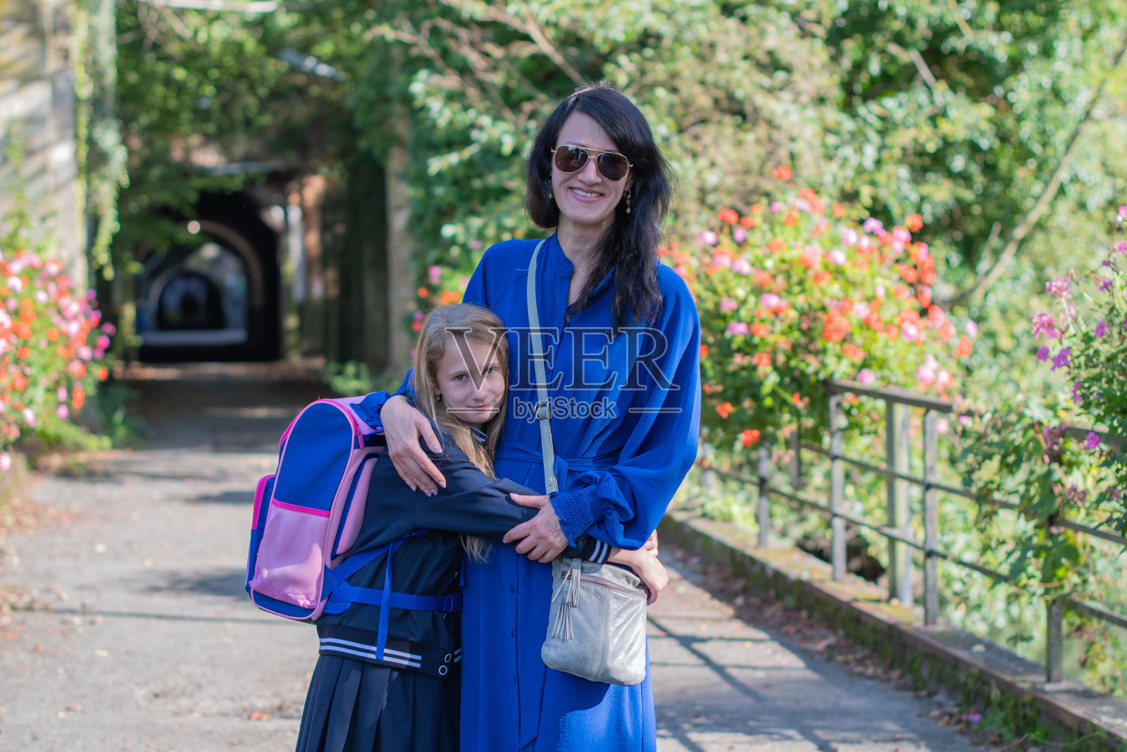 年轻的黑发女郎穿着蓝色的裙子陪着她的小女儿去学校，她们一起在公园散步，女孩亲切地拥抱着妈妈，回到学校照片摄影图片