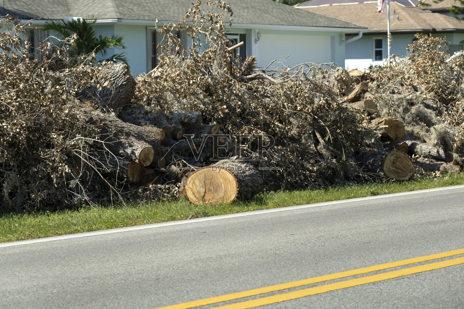 在居民区的街道上，成堆的被飓风刮下来的树枝和树枝残骸等待着救援卡车的到来。自然灾害的后果照片摄影图片