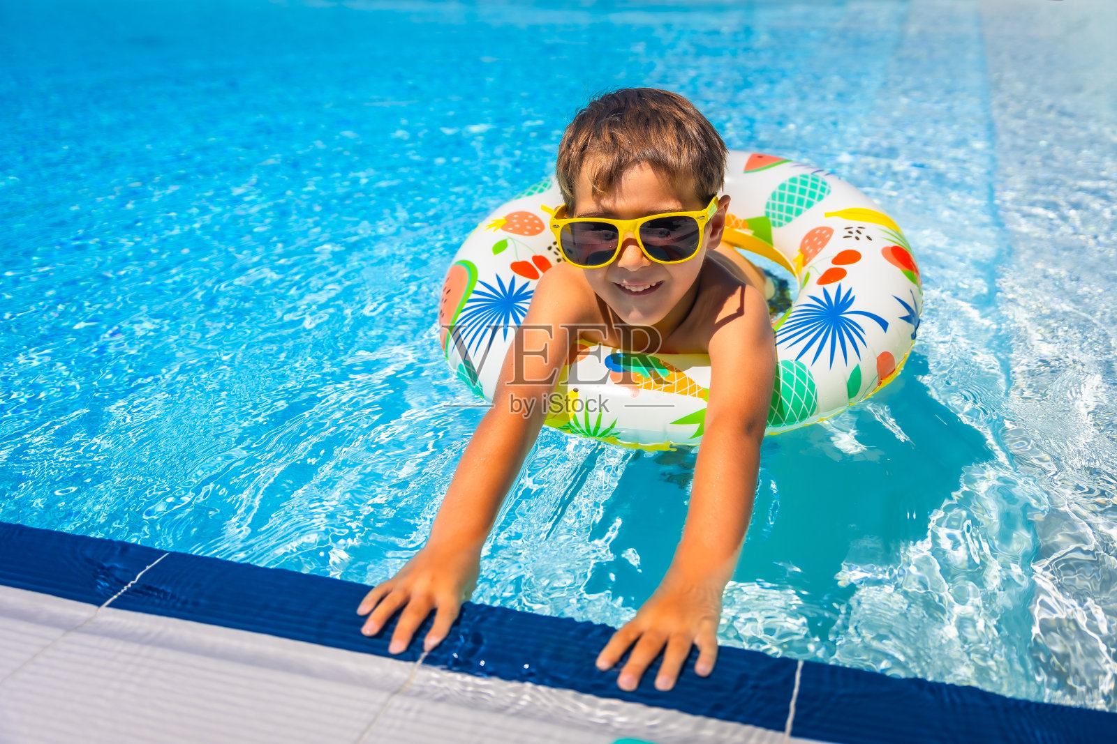 戴墨镜的男孩躺在游泳池的充气环上照片摄影图片