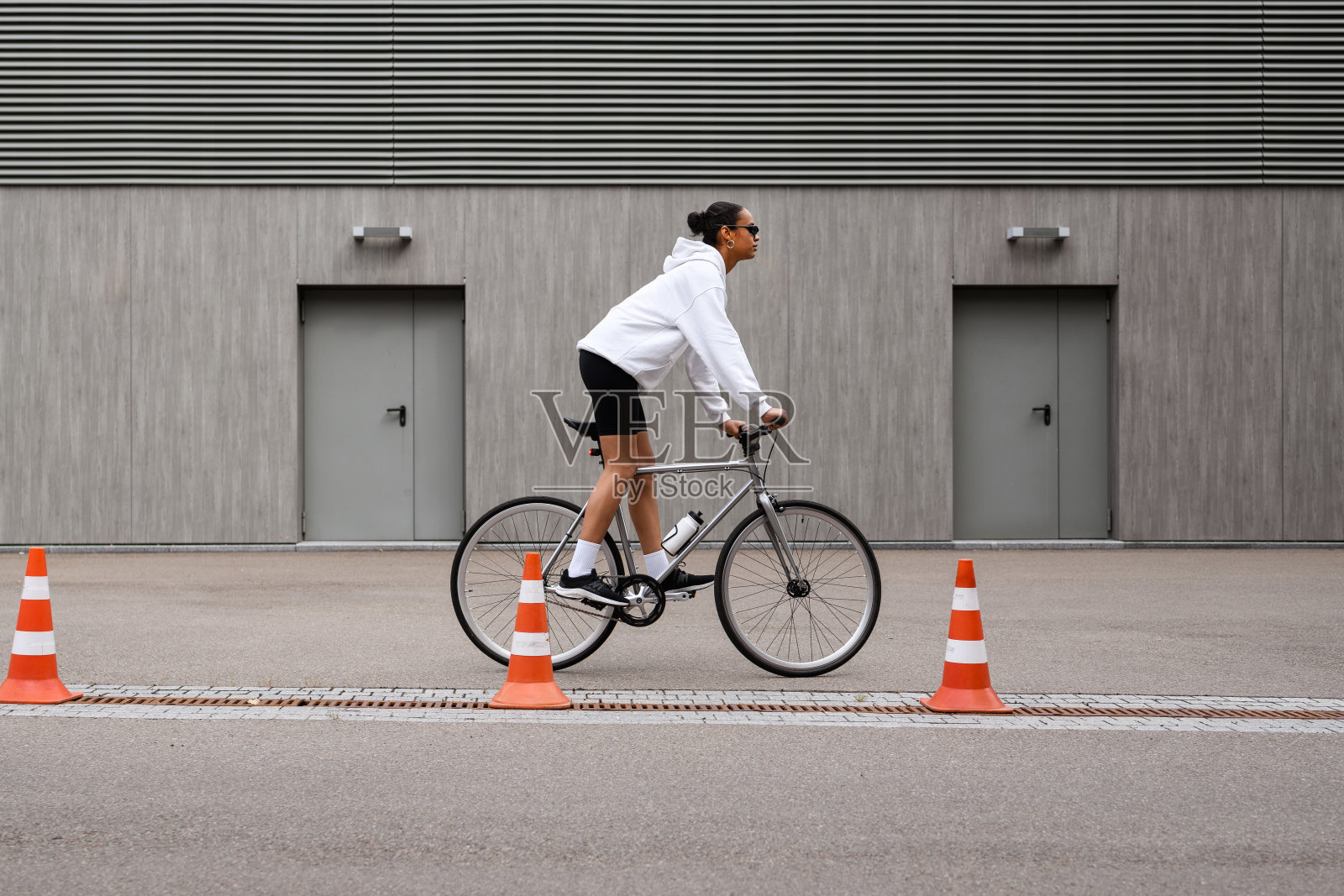 非裔美国妇女穿着连帽衫，戴着墨镜在街上骑自行车照片摄影图片