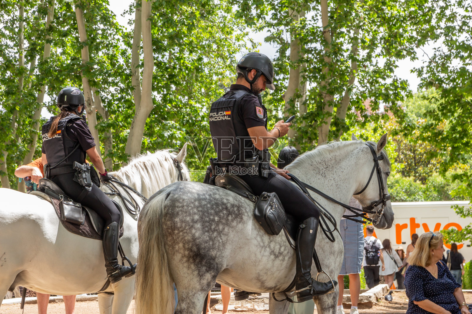 两名西班牙国家警察骑在马背上，其中一人正在使用手机，马德里照片摄影图片