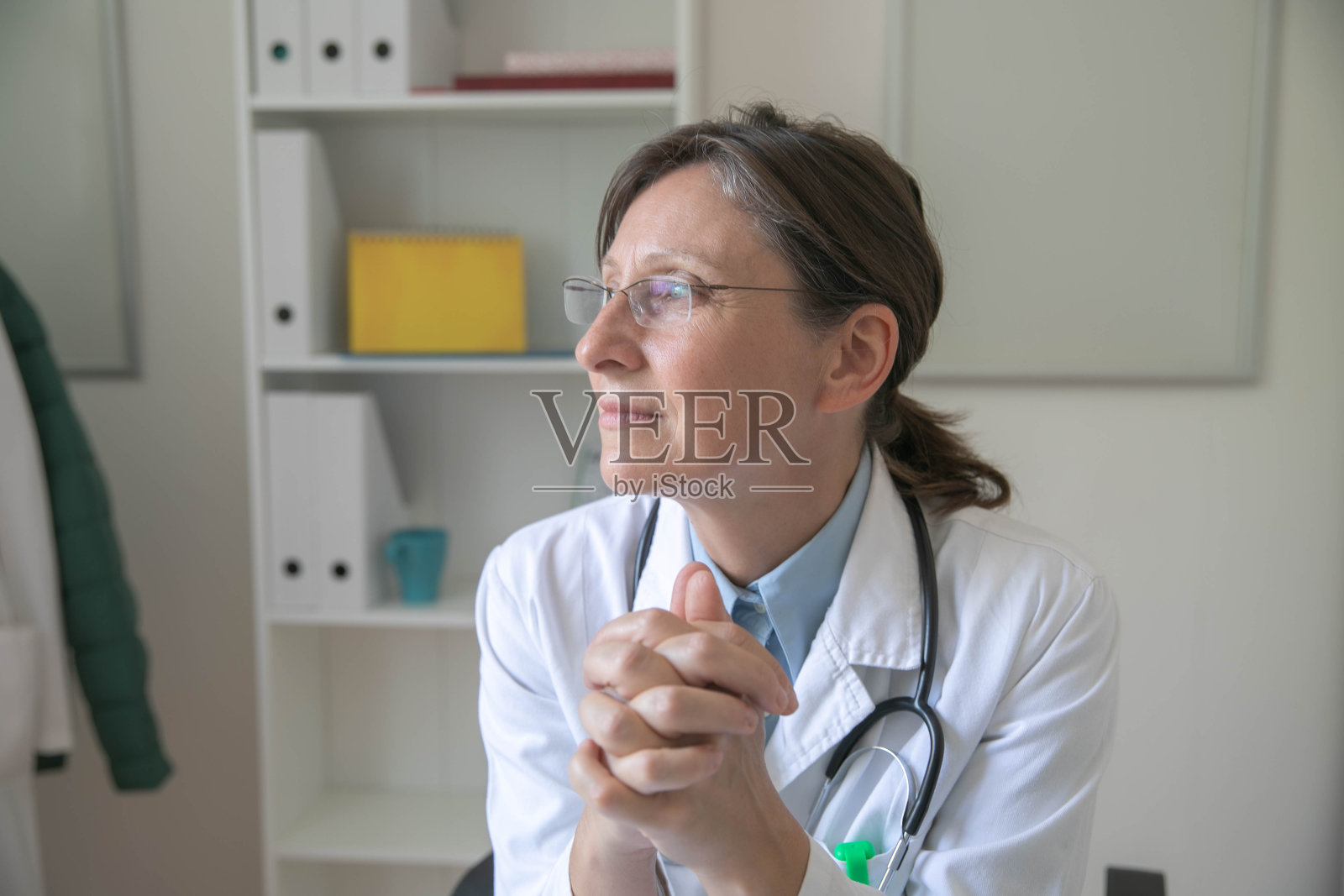 一位中年女医生坐在办公室的办公桌前，若有所思照片摄影图片