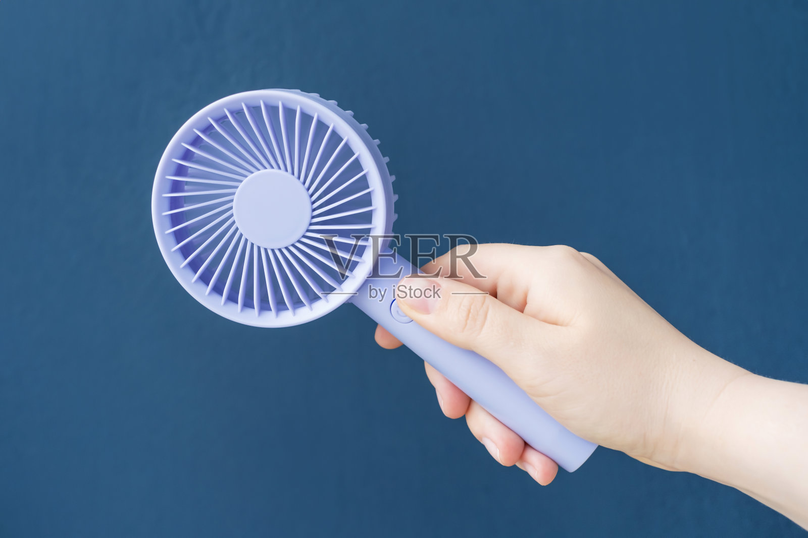 女性手持迷你风扇在蓝色背景的特写。照片摄影图片