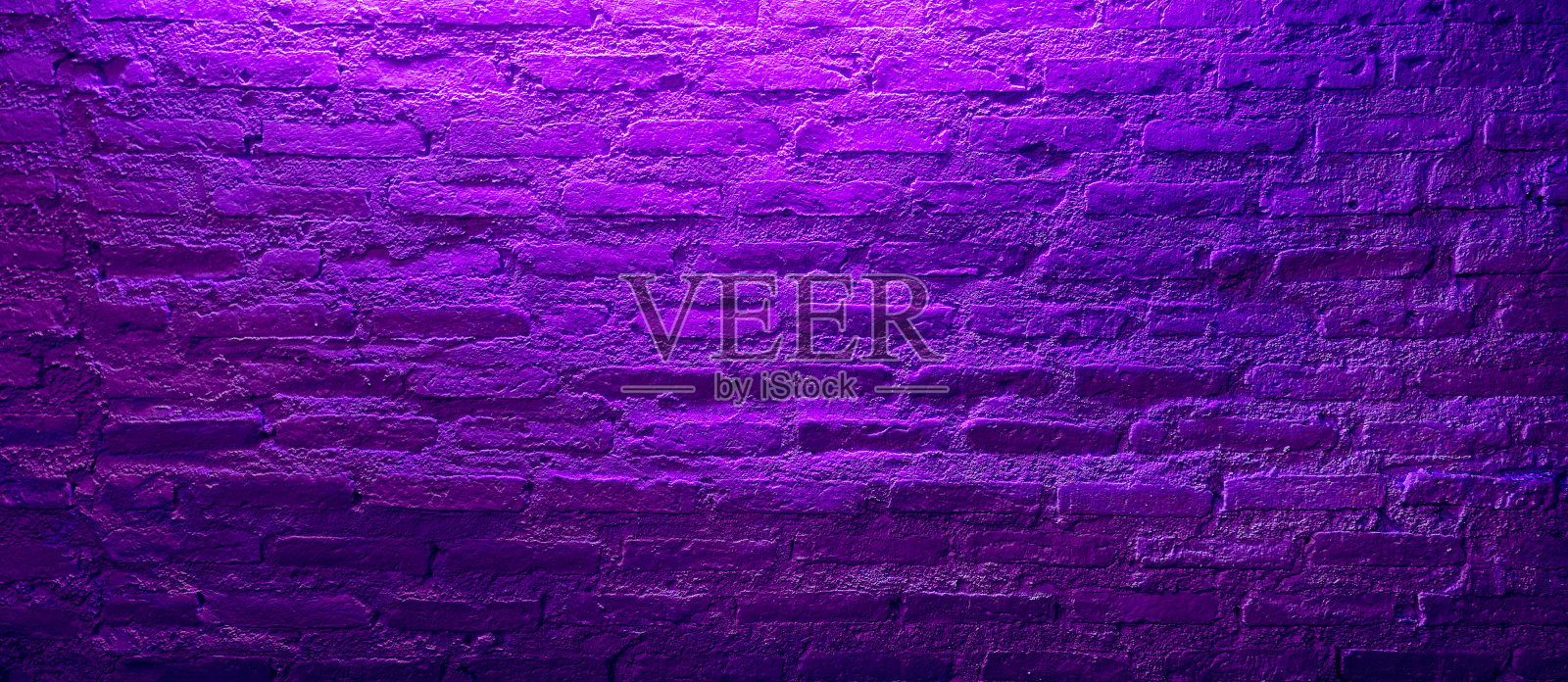 近距离的垃圾紫砖墙与霓虹紫光从上面的岩石风格。紫色的空砖墙被天花板上的光照亮。照片摄影图片