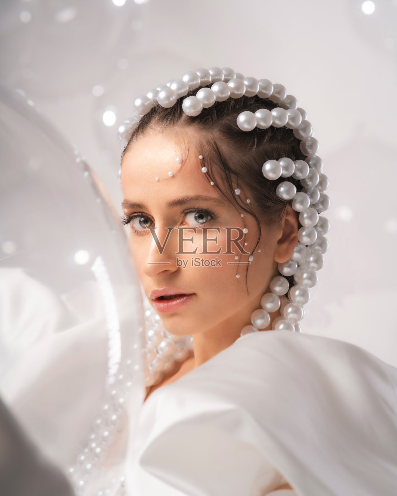 一个年轻美丽的女孩在白色的背景上穿着白色的裙子，头发上有球和珠子照片摄影图片