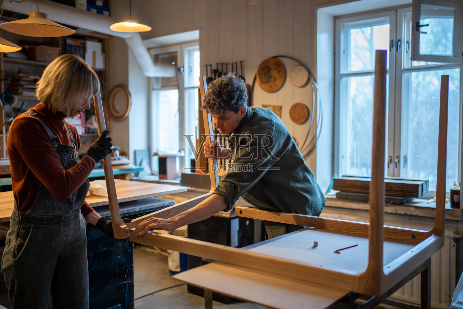 木工车间，工匠们一起工作。女人和男人组装工作台，连接部件照片摄影图片