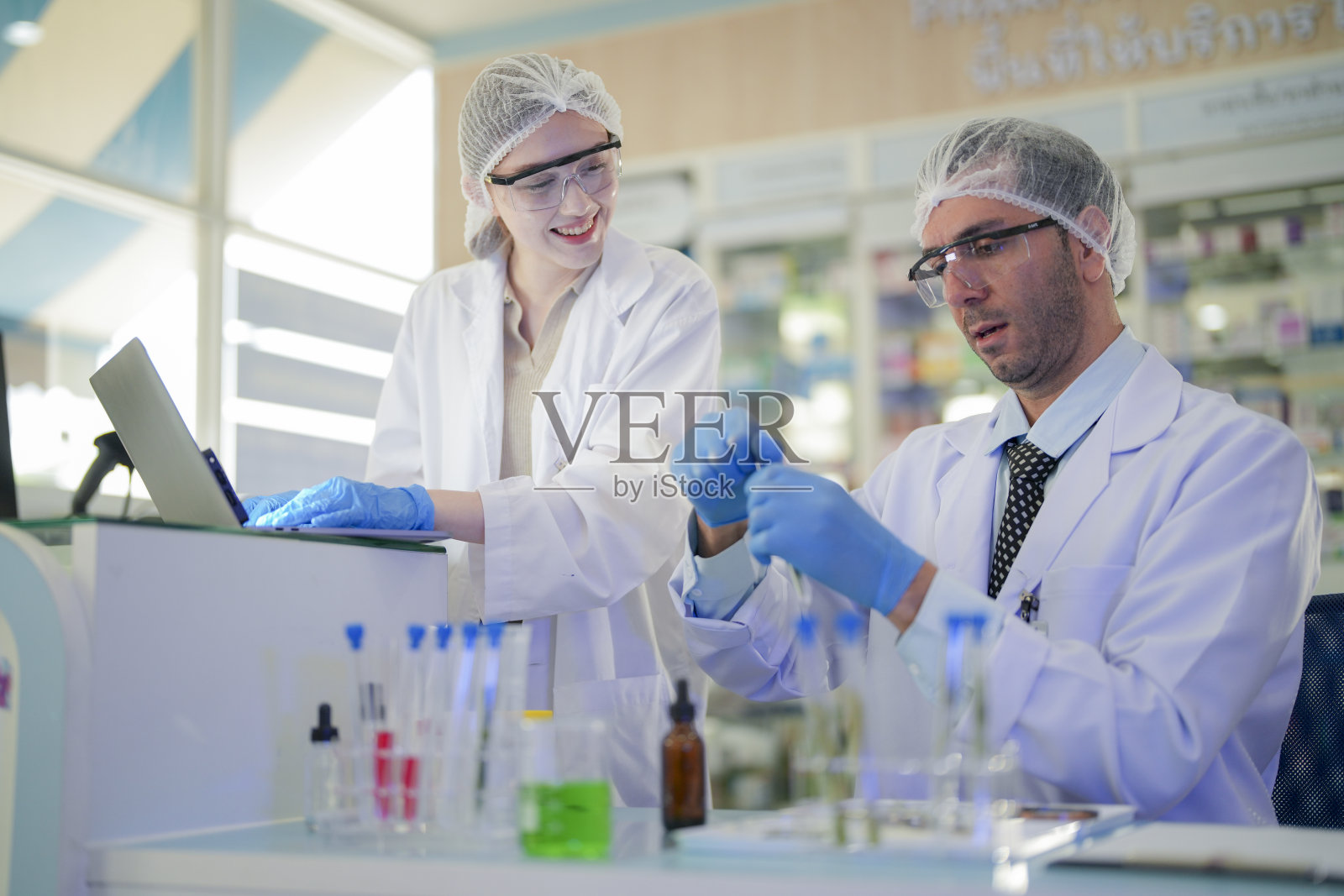 科学家进行实验并记录数据。人们为生产药物和生物化学而安排试管和化学品设备。人们拿着装有化学液体和植物样品的管子。照片摄影图片