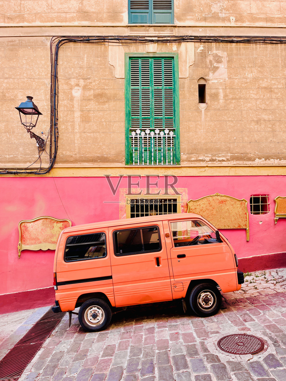 橙色巴士在老城区的小山上靠近绿色的窗户，粉红色和棕色的墙与路灯照片摄影图片