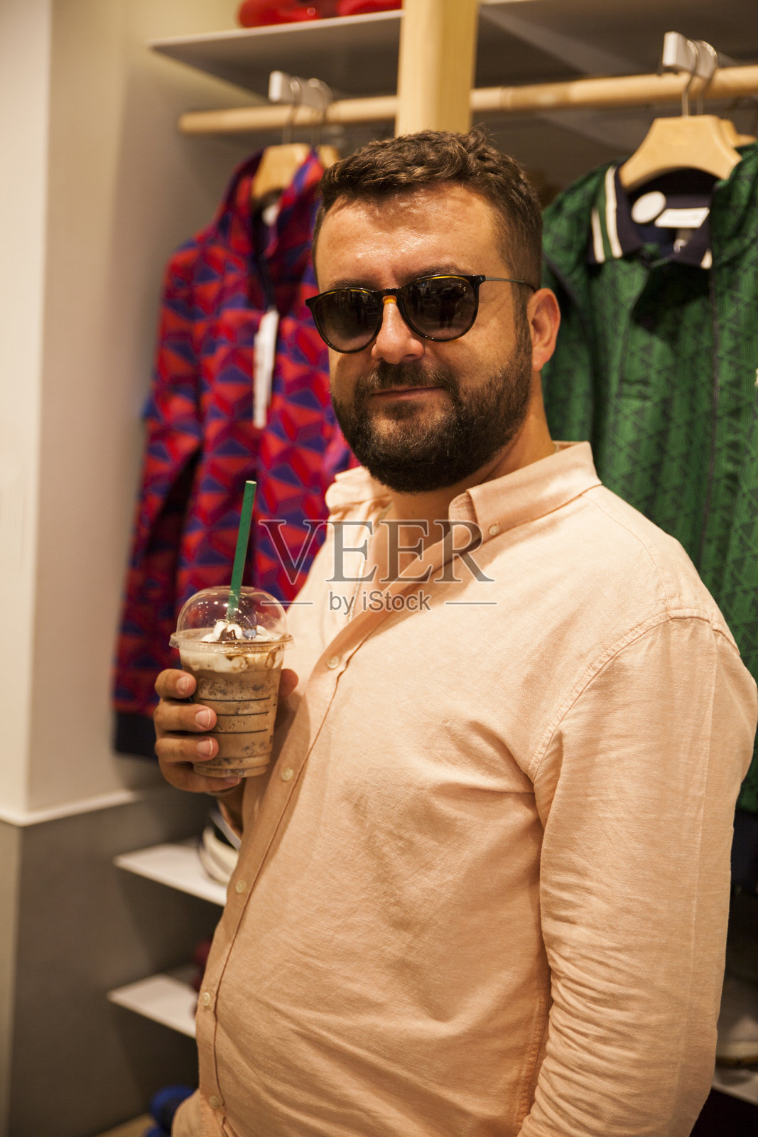 戴着黑眼镜的男人手里拿着咖啡在服装店里走来走去照片摄影图片