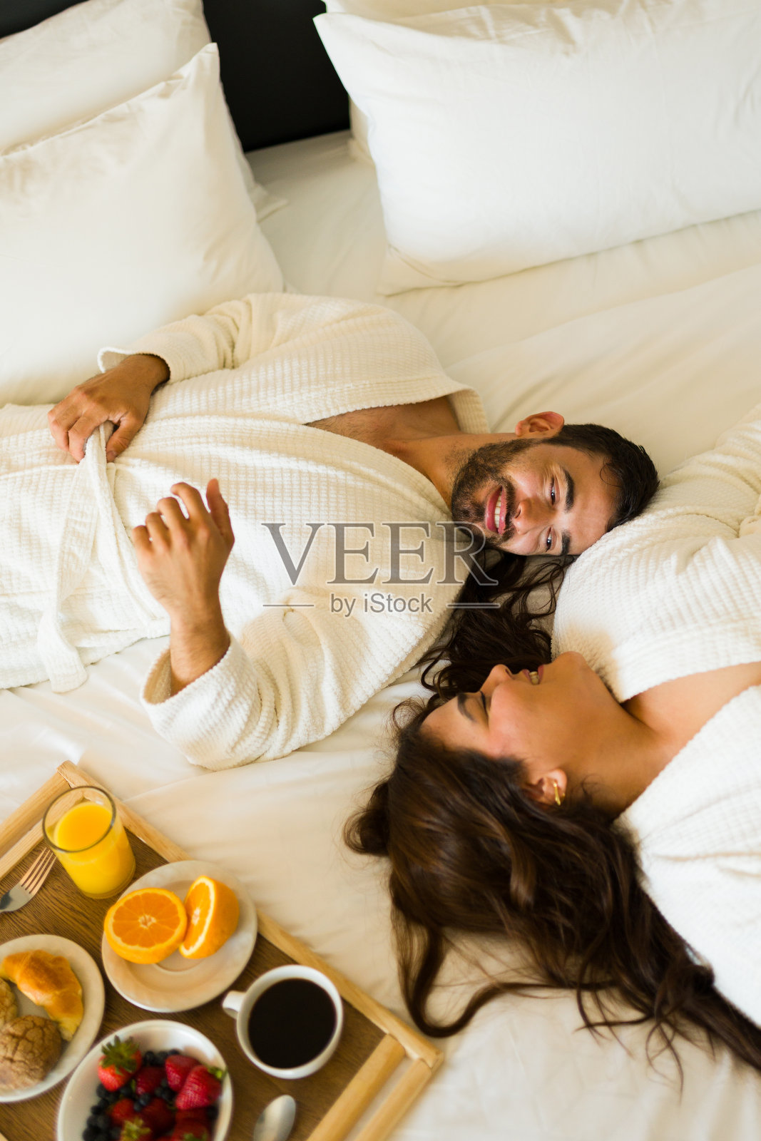 一对年轻夫妇在酒店度假期间在床上品尝浪漫的早餐照片摄影图片