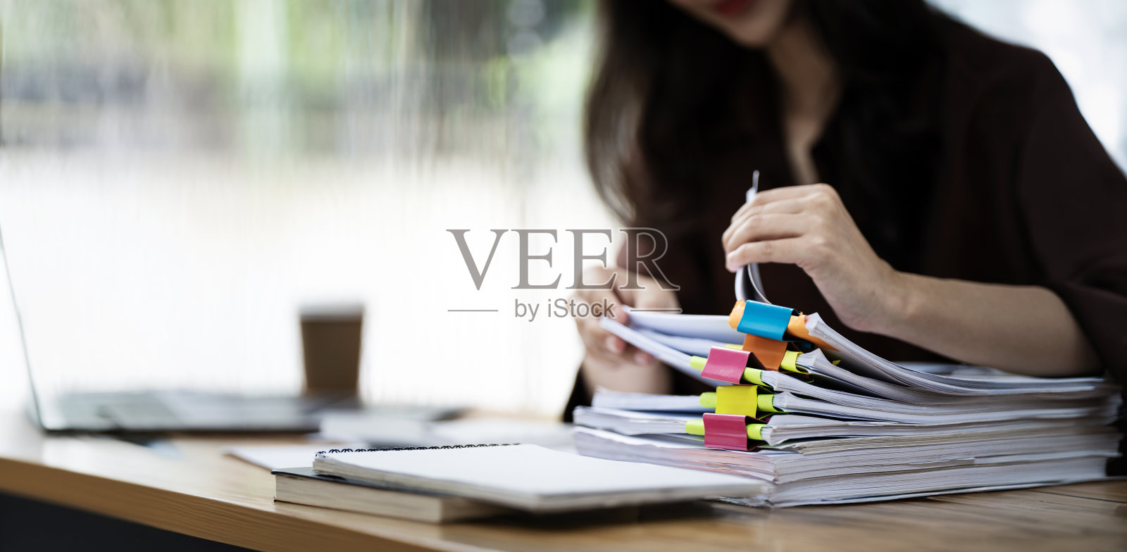 在繁忙的办公室里，女商人在成堆的纸质文件中工作，以便搜索和检查未完成的文件照片摄影图片