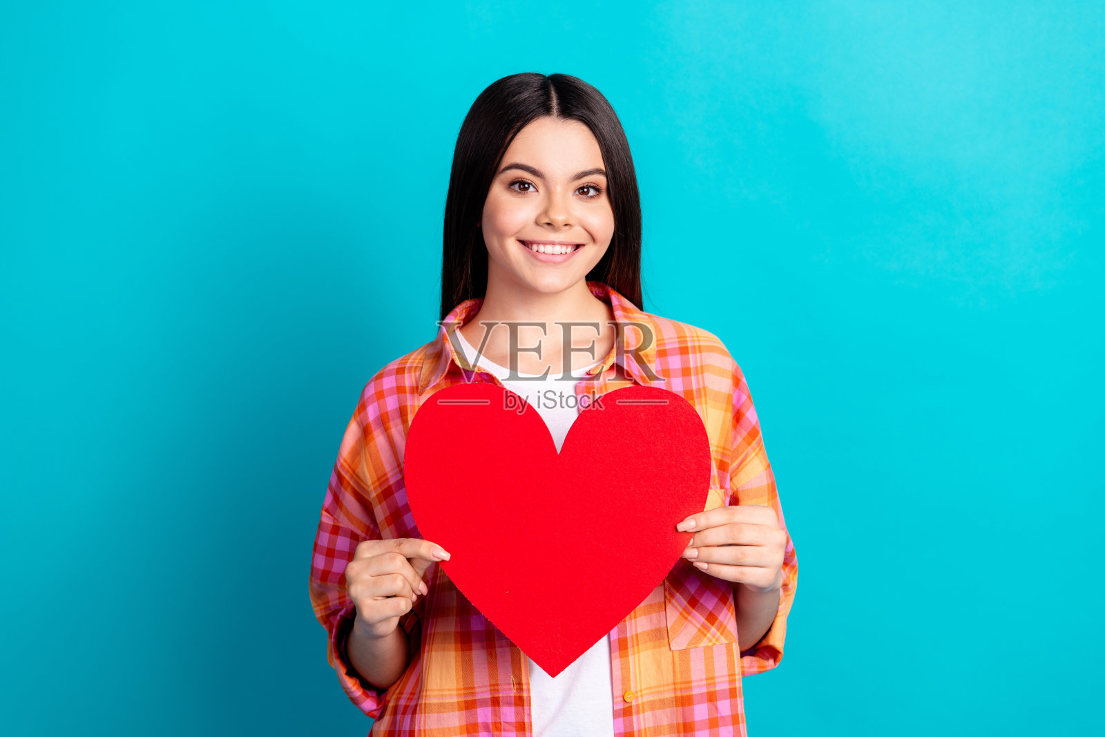 漂亮女孩的肖像拿着心卡，穿着格子衬衫，孤立在绿松石色的背景上照片摄影图片