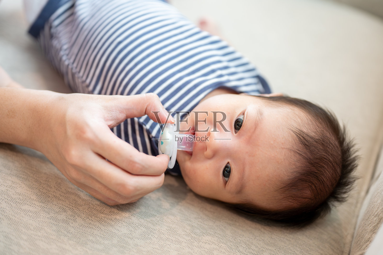 一个可爱的新生儿抱着奶嘴躺在沙发上。童年的概念照片摄影图片