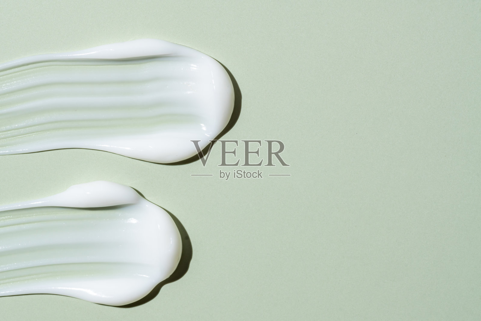 白色化妆霜纹理在绿色背景。护肤品涂抹。乳液，发膜或其他化妆品的纹理与复制空间照片摄影图片