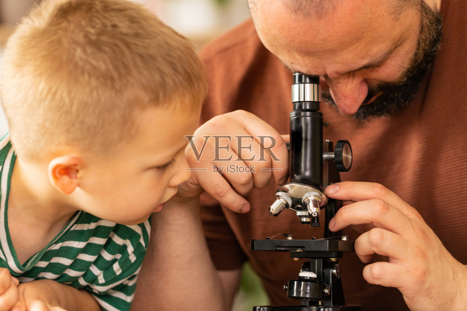 爸爸看显微镜的特写照片，他的儿子在旁边。照片摄影图片