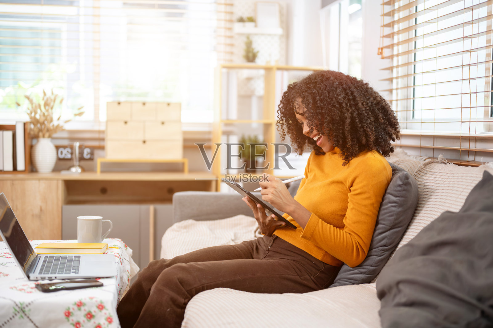 一个快乐的黑人妇女正在客厅的沙发上使用她的数码平板电脑。照片摄影图片