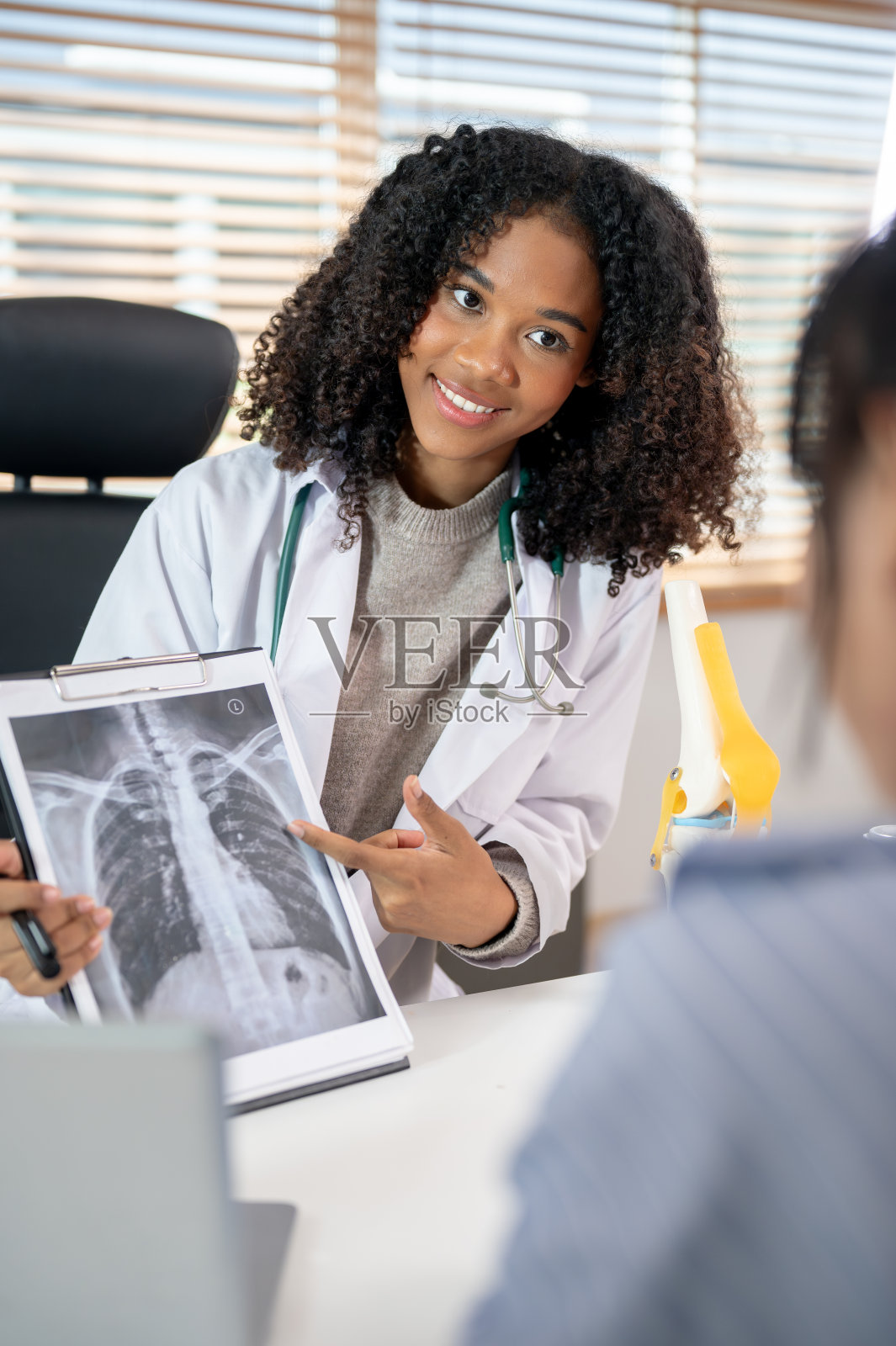 一位专业的黑人女性骨科医生向病人解释并展示肺部x光片。照片摄影图片