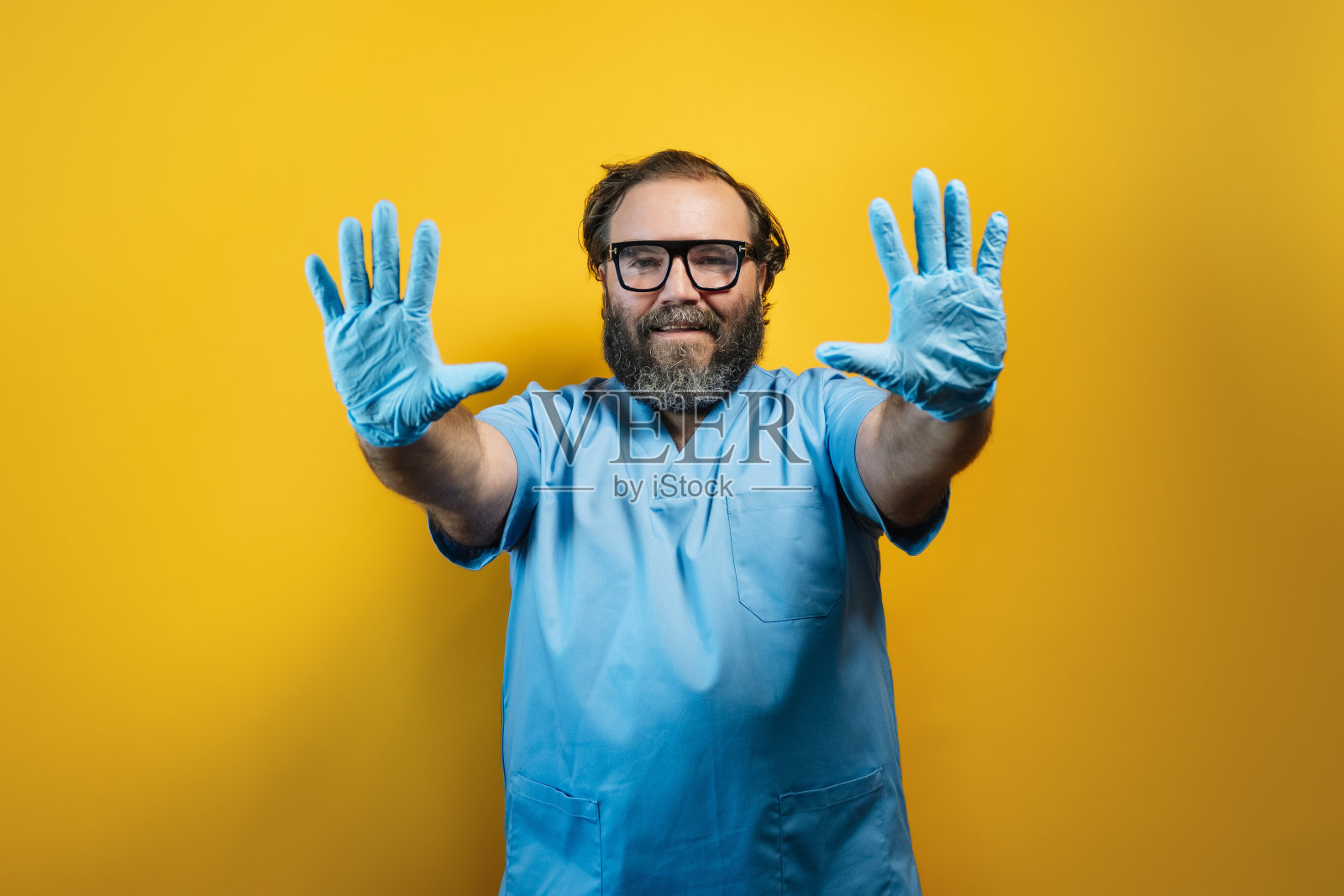 在黄色背景上穿着蓝色外套的医生用乳胶手套做手势。照片摄影图片