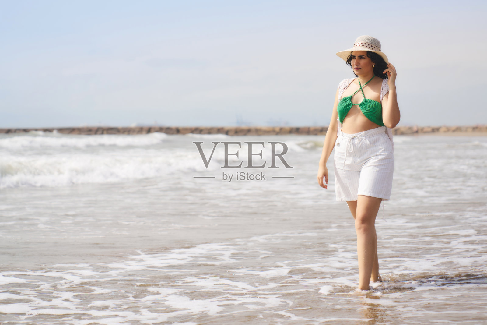 一个女人穿着绿色比基尼和白色短裤走在沙滩上照片摄影图片