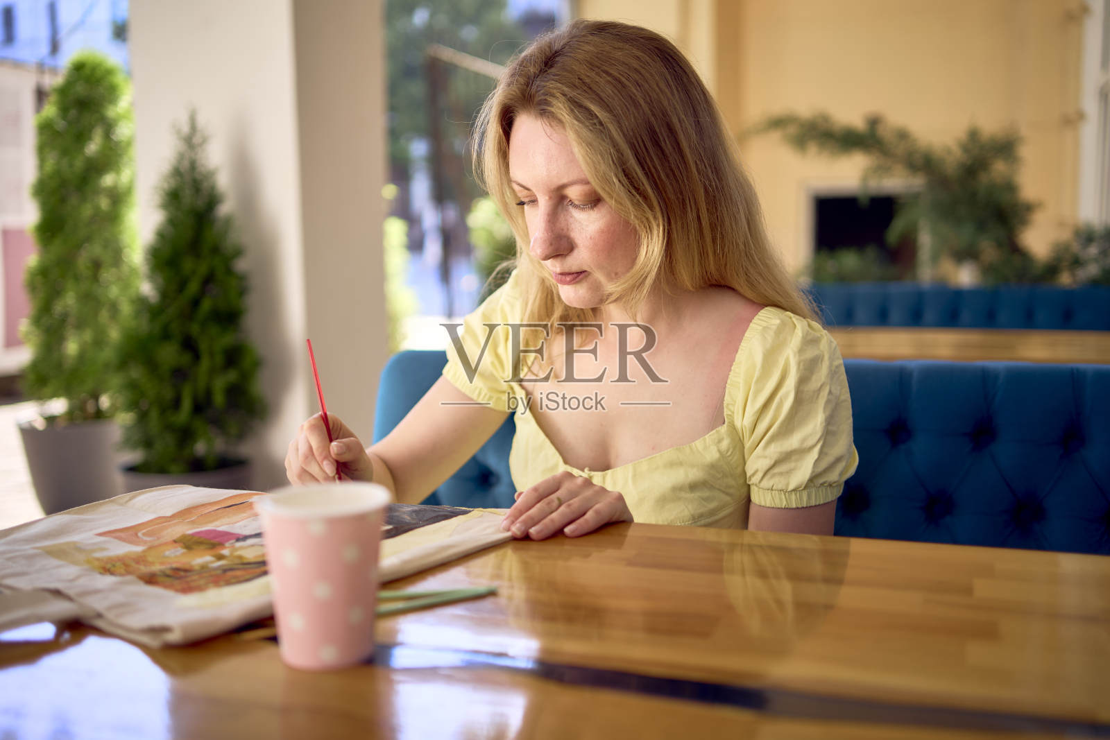 一位穿着黄色连衣裙的年轻漂亮的艺术家正在画一个定制的购物袋照片摄影图片