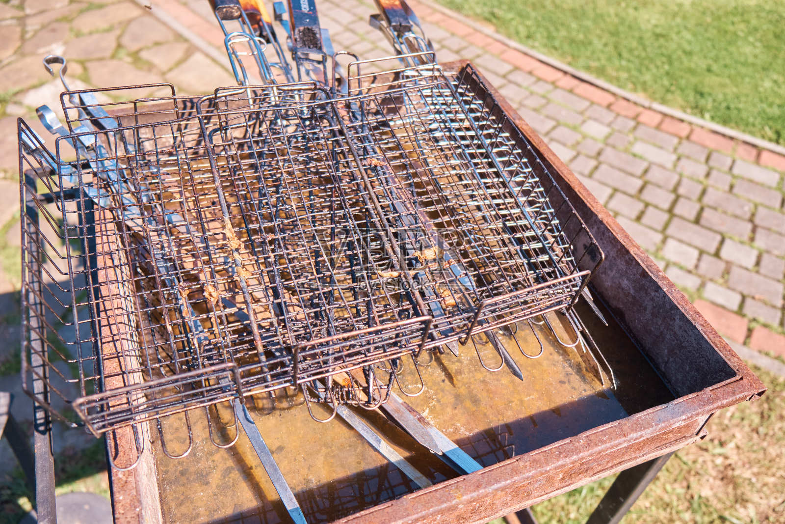 锈迹斑斑的旧铁制火盆，铁制肮脏的烧烤格栅和烤肉串在夏天绿草旁边的地上。有选择性的重点照片摄影图片