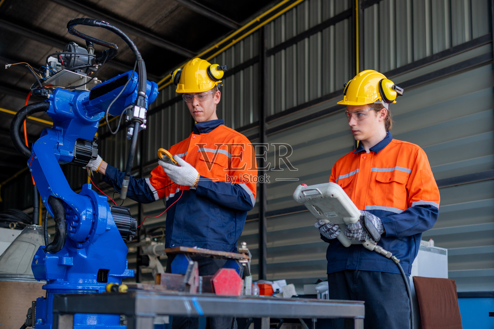 一群男工程师工人在暗室工厂里维护自动机械臂机。工人检查和修理自动机械手。戴安全眼镜和安全帽的工人。照片摄影图片