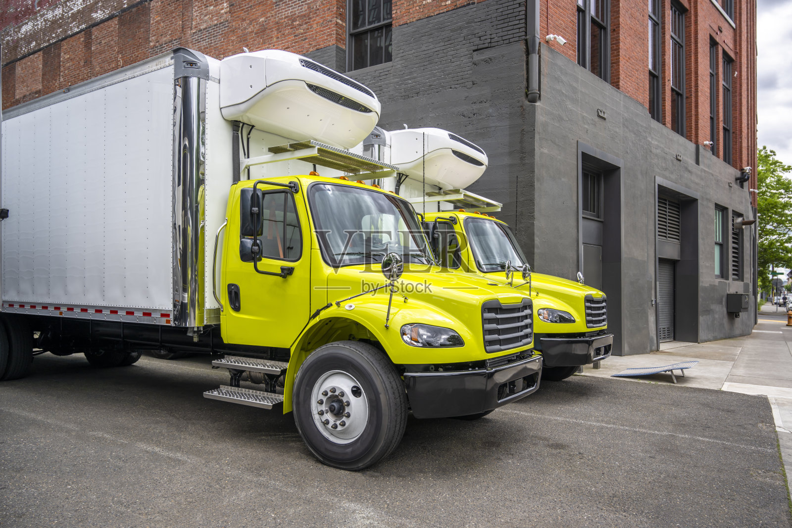 城市街道上的仓库停车场上，停着两辆带冷藏箱拖车的出租卡车照片摄影图片