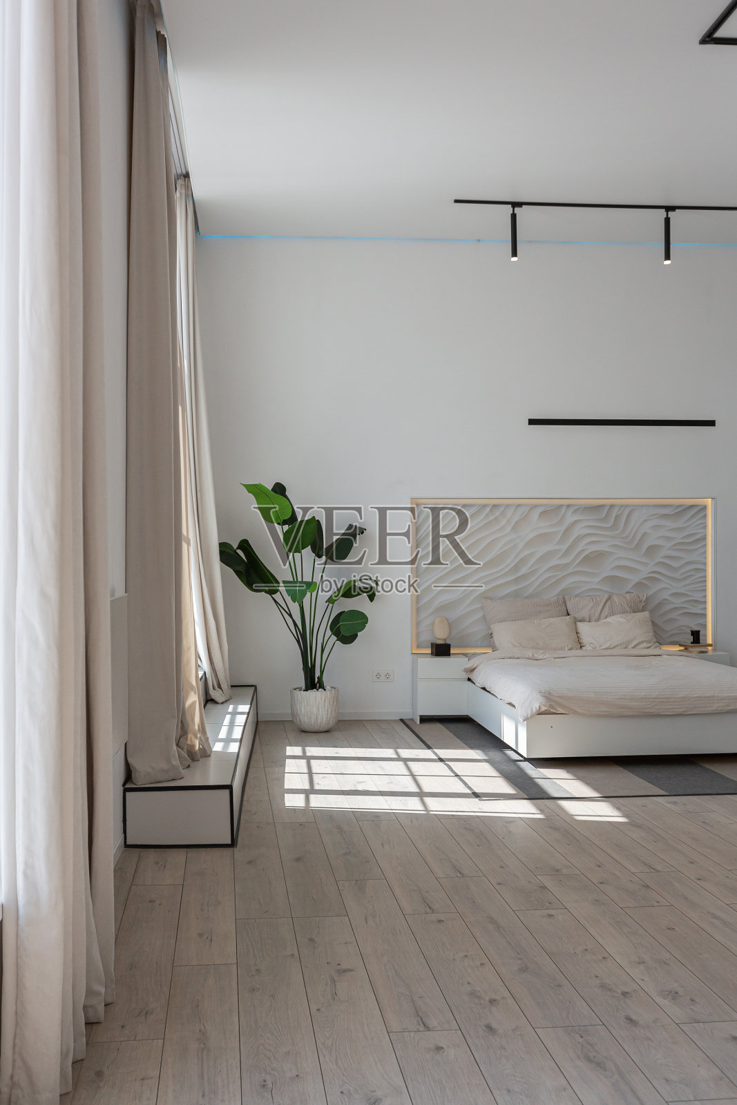 卧室区在一个极简主义的现代豪华设计的昂贵的房子在一个阳光明媚的日子。在床头板的装饰板上，白色的墙壁上有灰泥、镶木地板，没有灯饰和装饰灯照片摄影图片