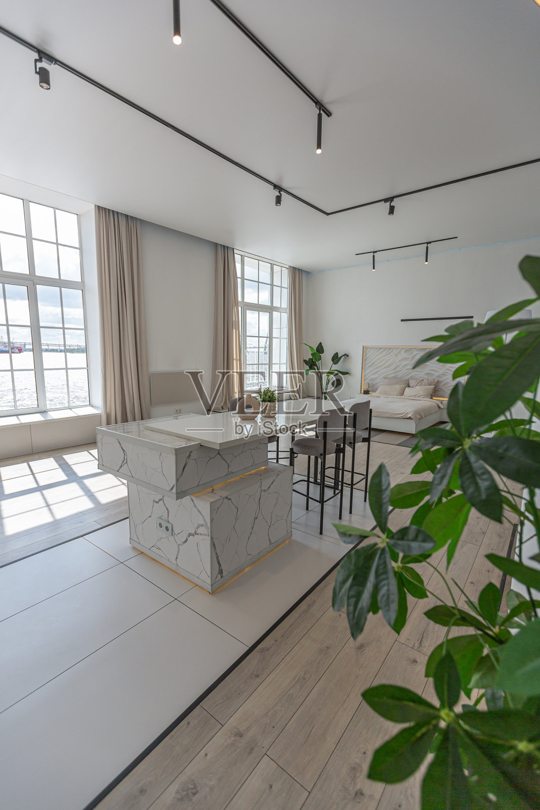 厨房和餐厅岛与高酒吧凳在一个极简主义的现代豪华设计昂贵的房子在一个阳光明媚的日子。白色的墙壁，石膏，镶木地板，装饰照明，里面没有人照片摄影图片