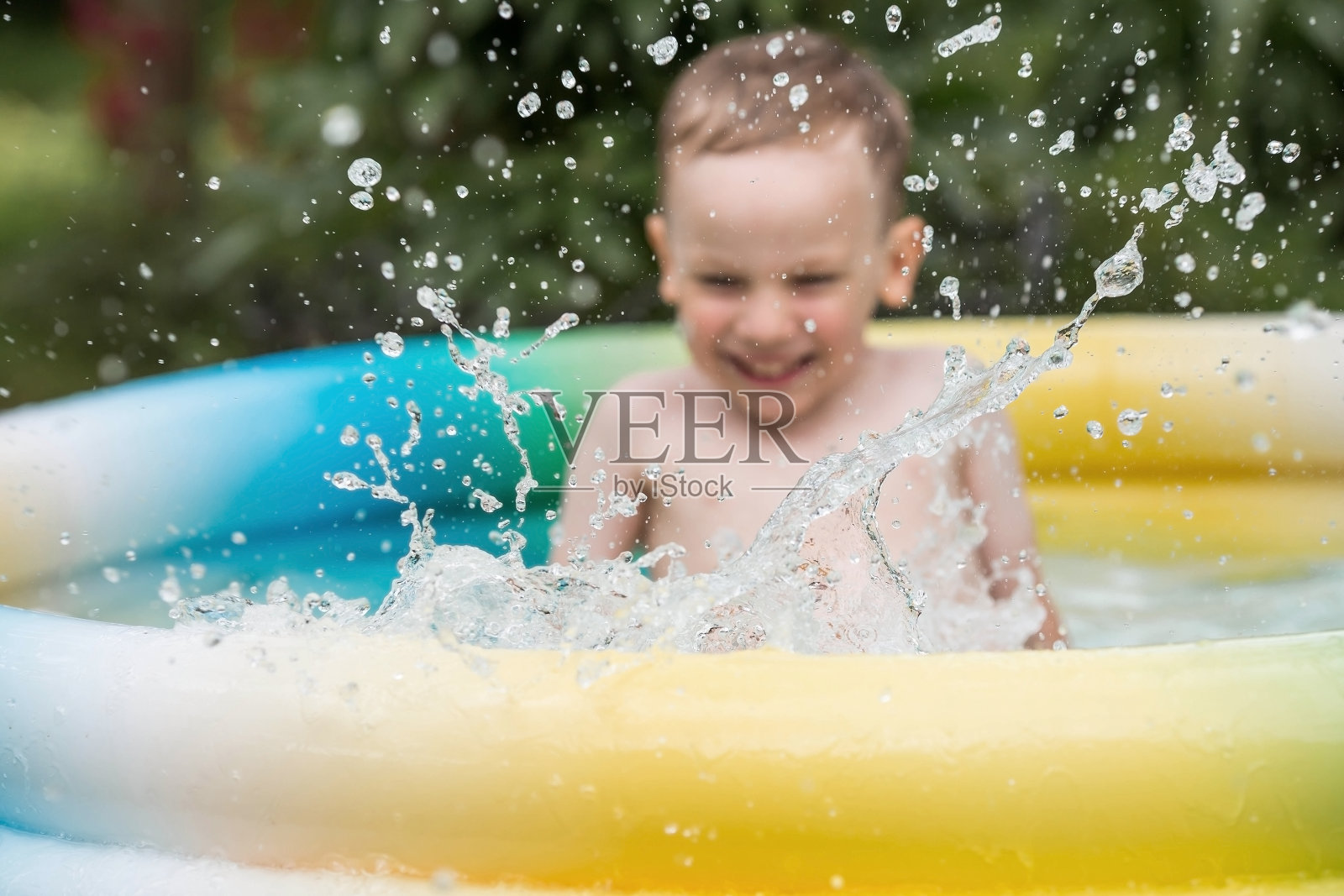 天气很热。一个可爱的男孩正在游泳池里游泳和溅水花。一个快乐的小男孩对着镜头微笑。水花四溅。暑假带孩子的概念。照片摄影图片
