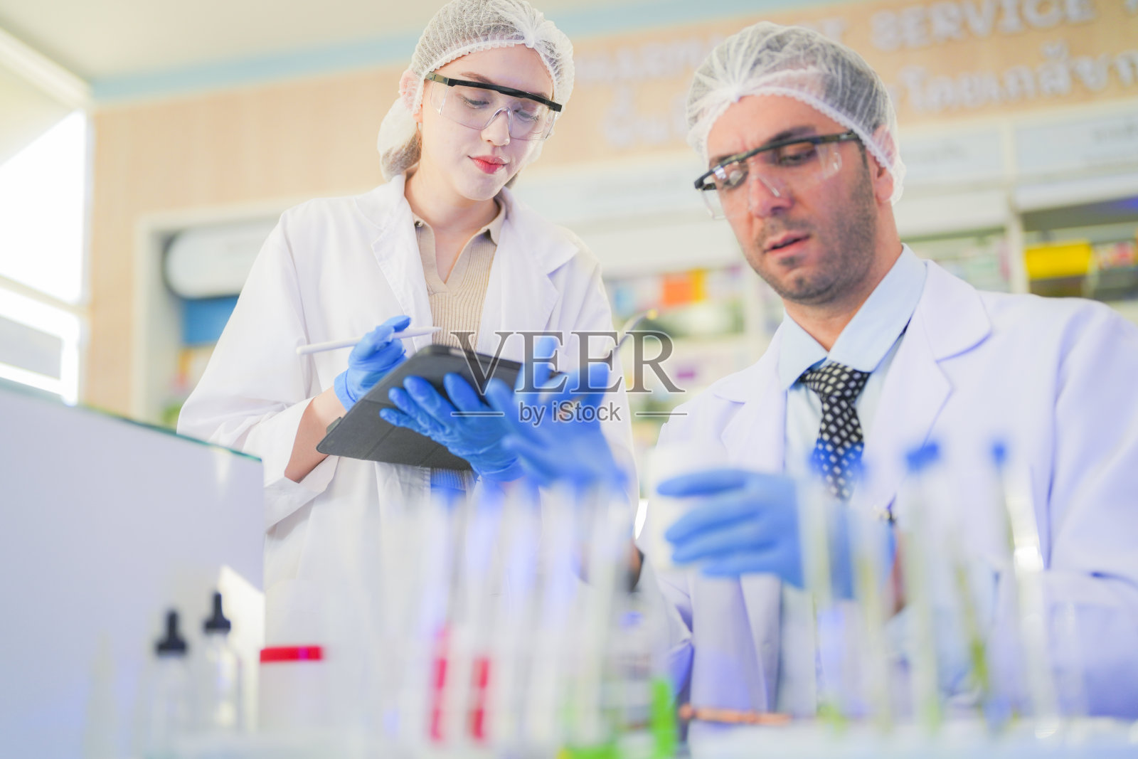 科学家进行实验并记录数据。人们为生产药物和生物化学而安排试管和化学品设备。人们拿着装有化学液体和植物样品的管子。照片摄影图片