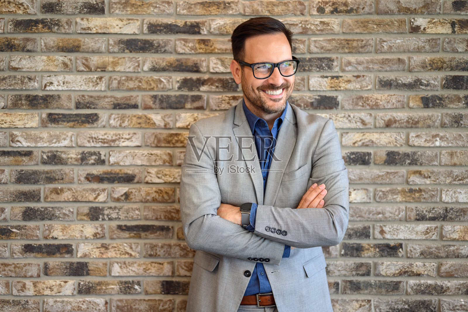 乐观的商人肖像，双臂交叉，对着办公室里的砖墙微笑照片摄影图片