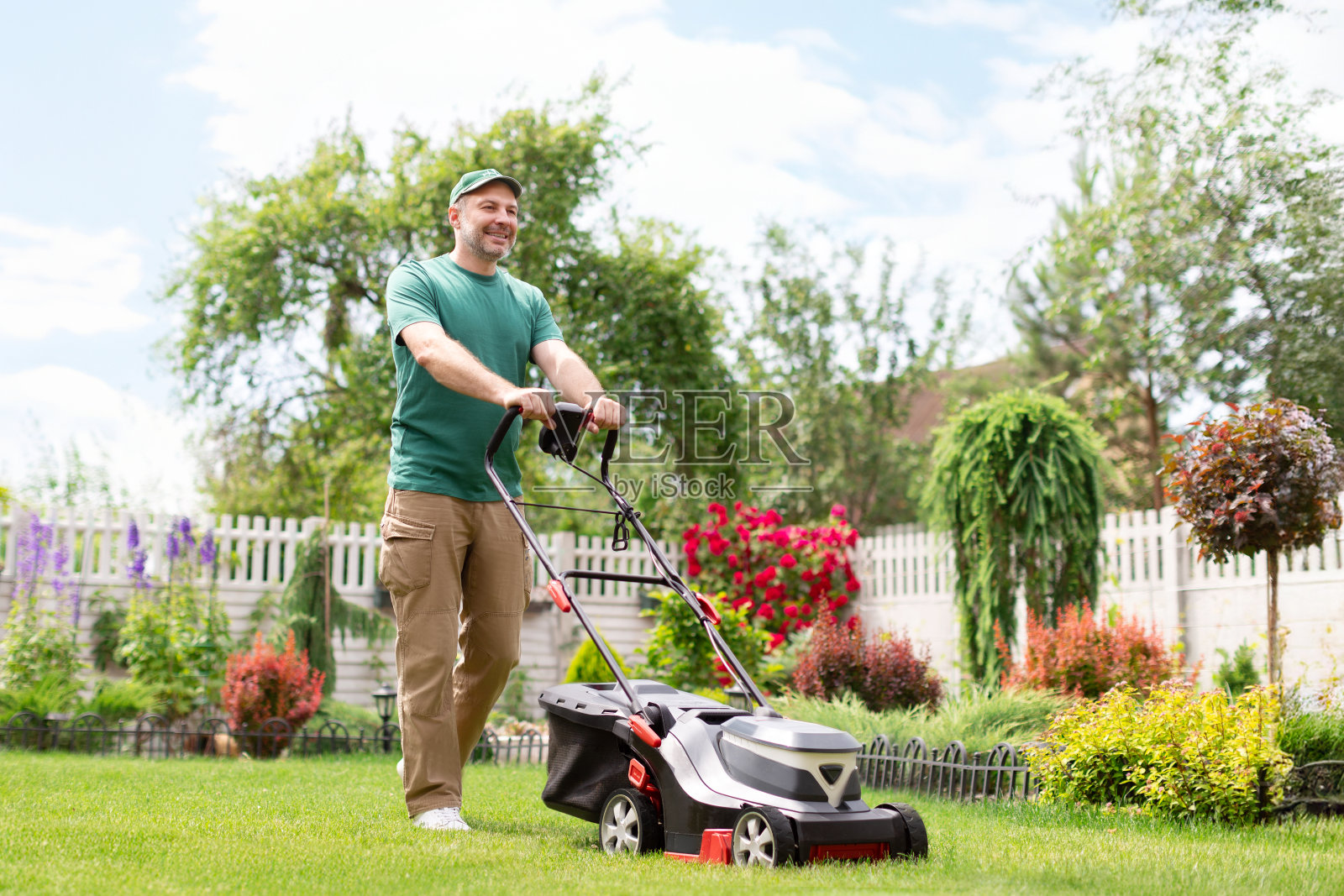 积极的人割草坪使用电动割草机在后院附近的乡村房子，全长，自由的空间照片摄影图片