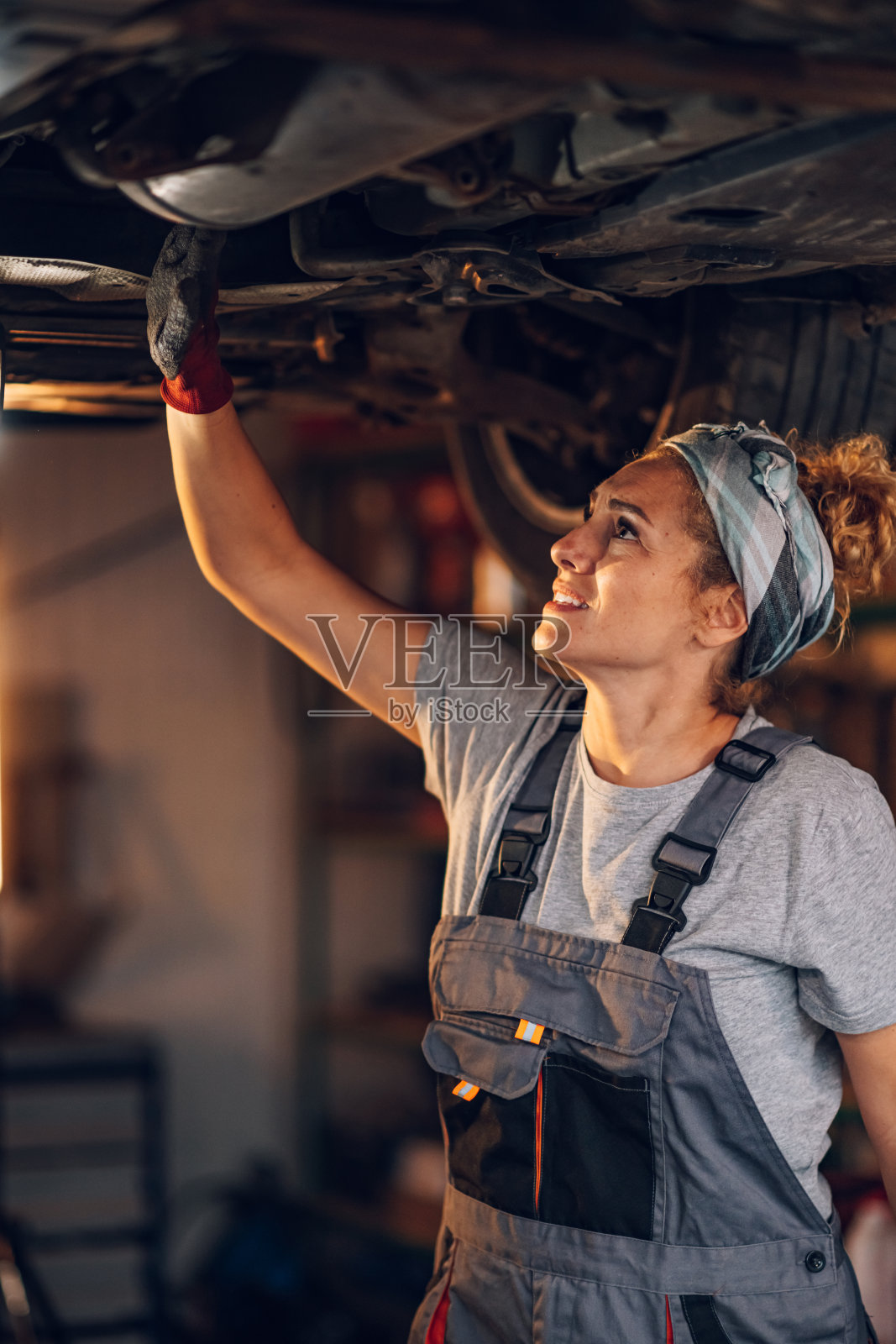 专注的女维修车间工人在吊车下检查问题。照片摄影图片