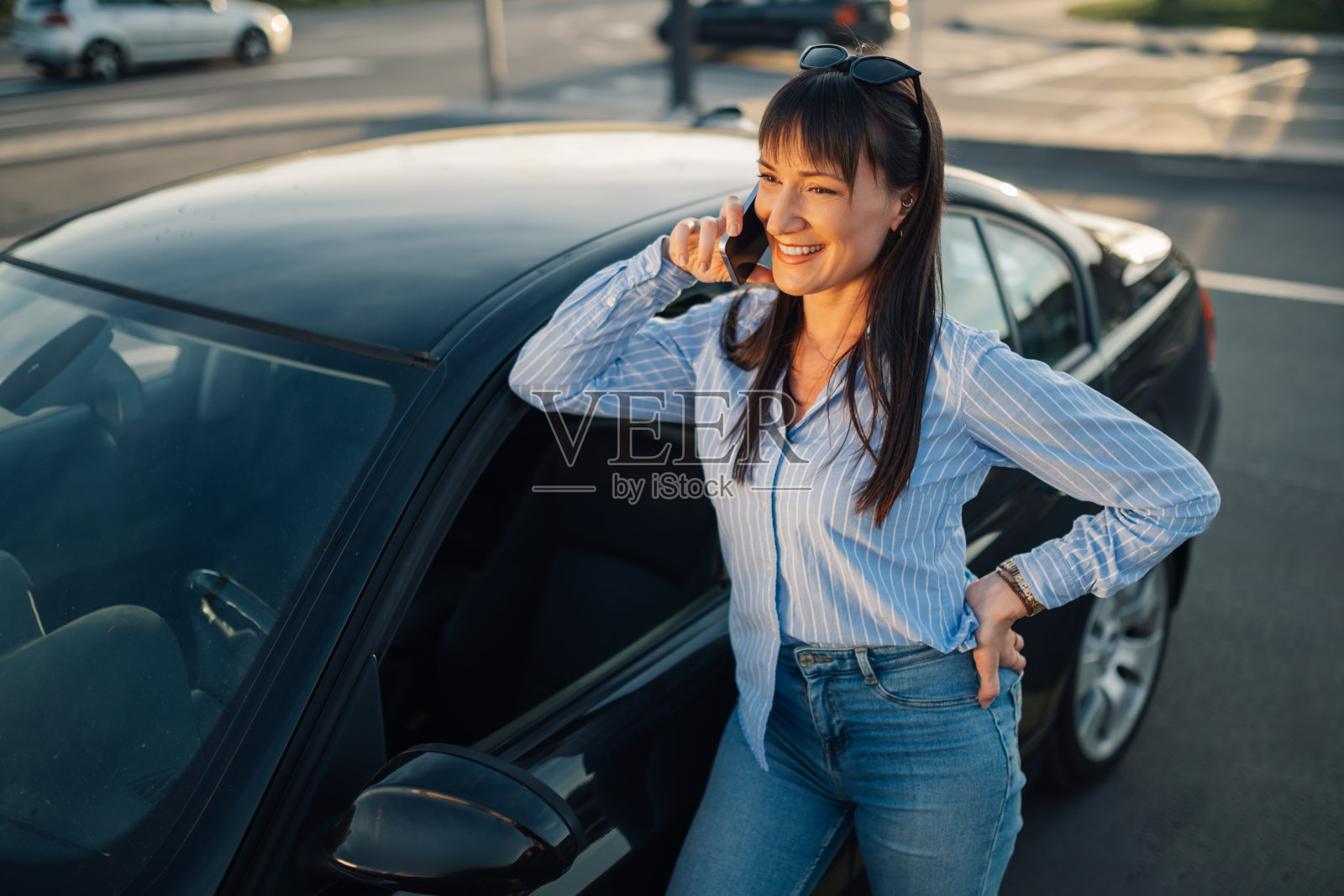 年轻快乐的女人站在停车时的汽车旁打电话照片摄影图片
