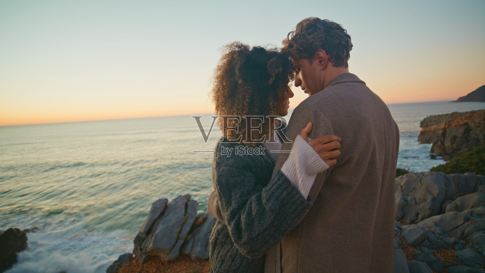 卷发女孩拥抱男友在黄昏海岸特写。拥抱在一起的恋人照片摄影图片