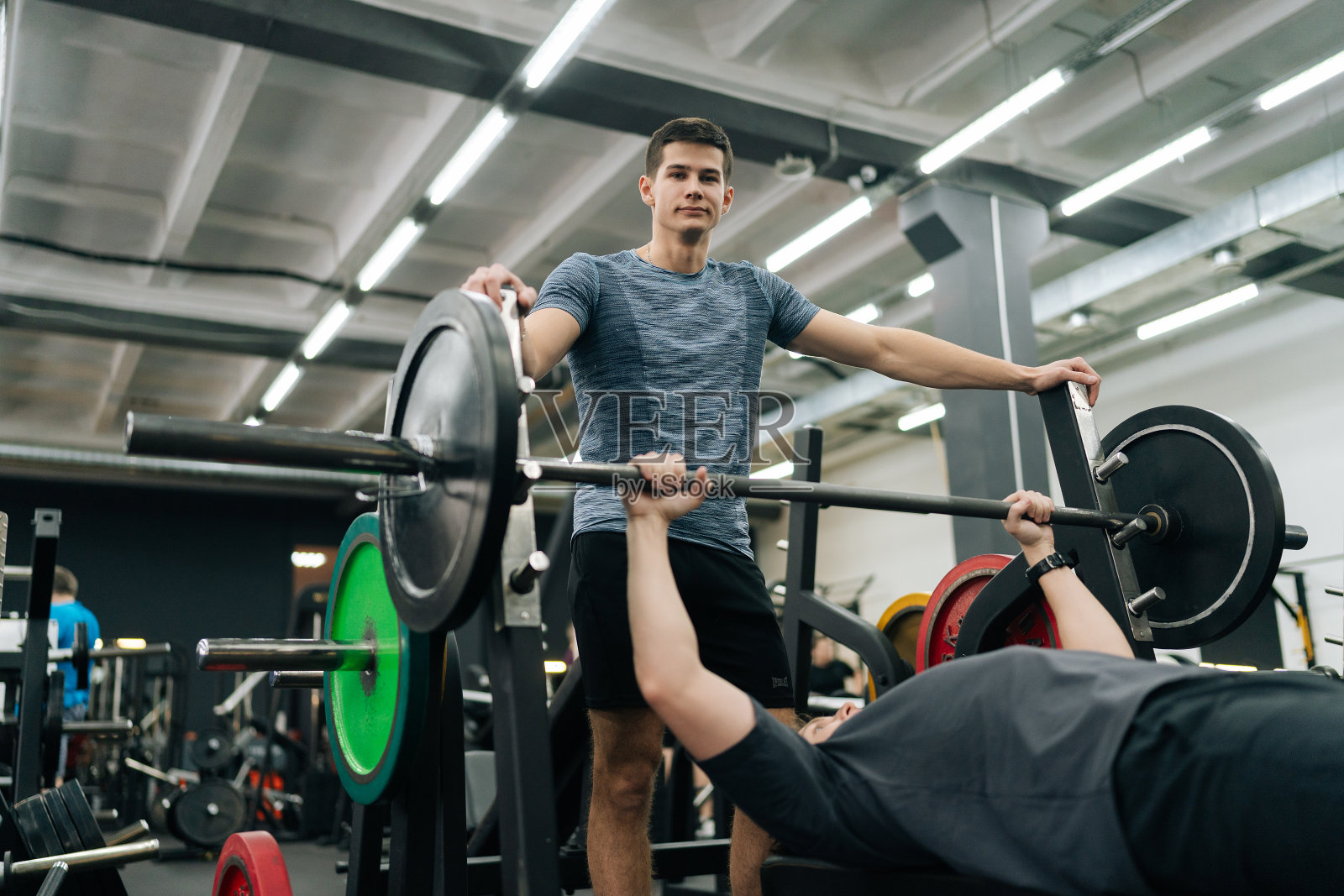 在健身房里，在私人教练的注视下，专注的初级男运动员在做倾斜卧推。健壮的年轻人在锻炼胸部肌肉照片摄影图片