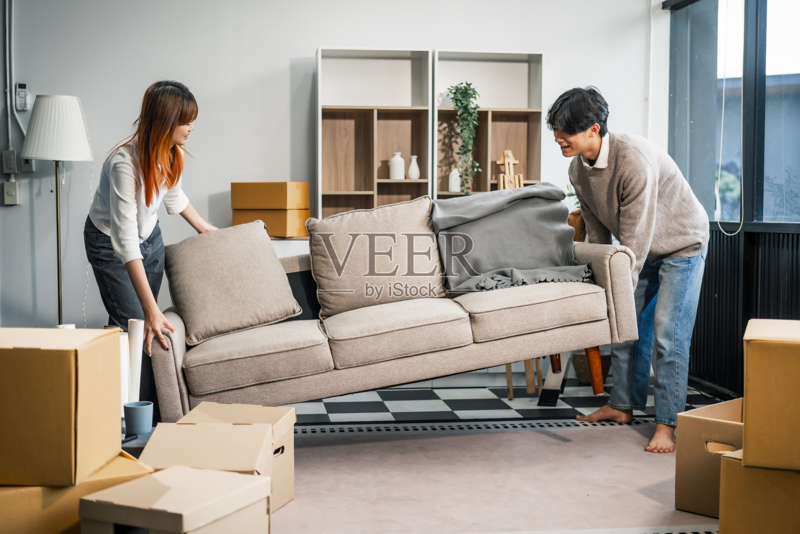 一对年轻夫妇愉快地在新家一起搬家具。他们像一个团队一样工作，搬运箱子和物品，营造出一种快乐的家庭氛围。照片摄影图片