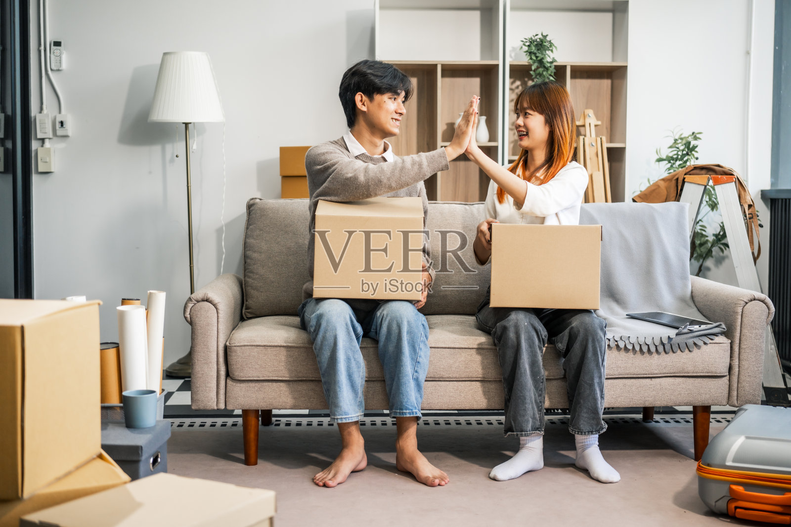 一对年轻夫妇愉快地坐在沙发上，把他们的东西装进一个大箱子里，准备搬到新家去。他们分享微笑和兴奋，准备一起开始新的生活。照片摄影图片