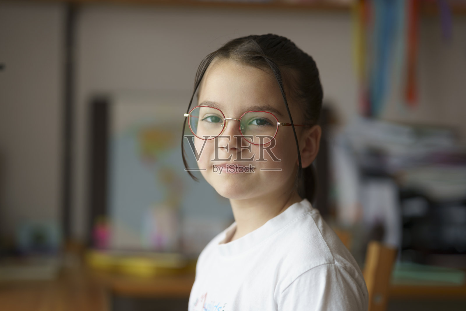 一个年轻漂亮的小女孩，戴着眼镜，梳着发型，坐在钢琴旁。背景中模糊了孩子们的房间。童年教育理念照片摄影图片