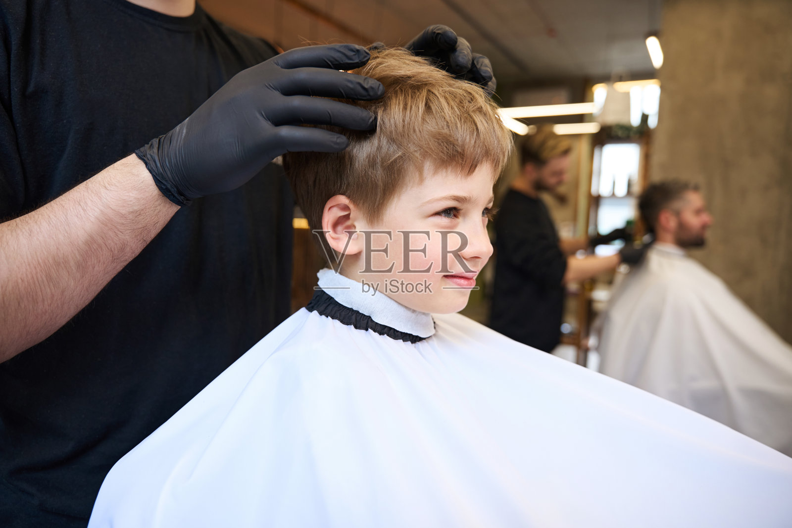 有资格的理发师按摩小男孩客户的头部和造型发型照片摄影图片