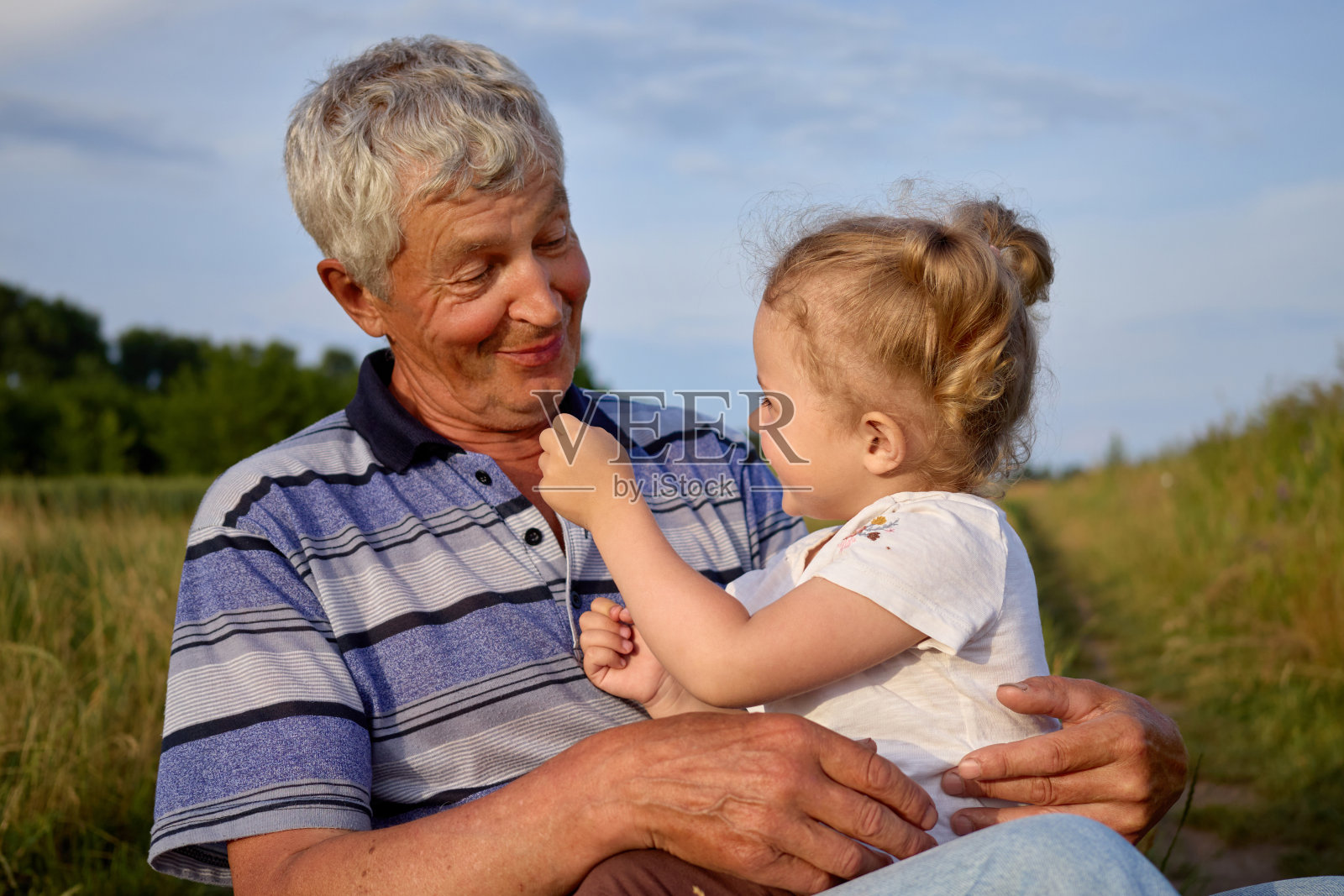 一个开朗的男人和他的孙女在夏日的田野里休息，在开阔的乡村环境中感受着爱和幸福，在田野里享受着休息照片摄影图片