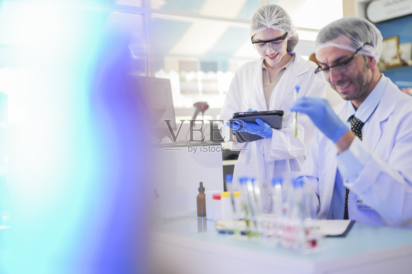 科学家进行实验并记录数据。人们为生产药物和生物化学而安排试管和化学品设备。人们拿着装有化学液体和植物样品的管子。照片摄影图片