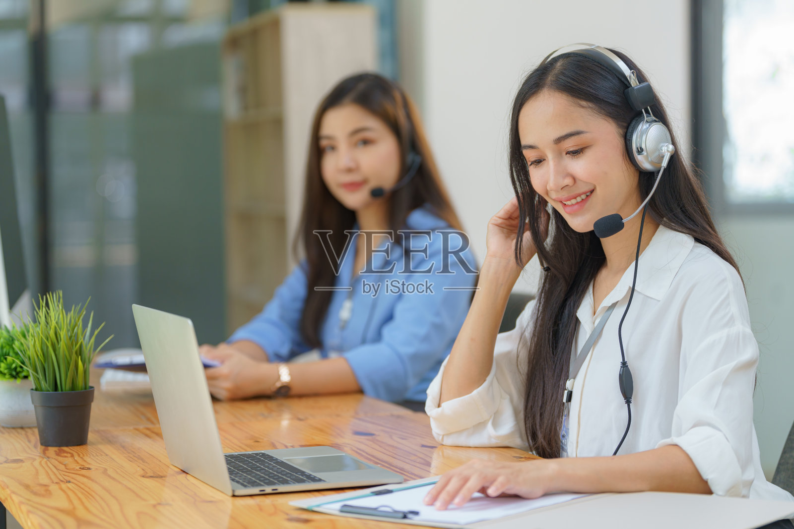 快乐微笑的接线员亚洲女性客户服务代表戴着耳机在呼叫中心的电脑上工作。照片摄影图片