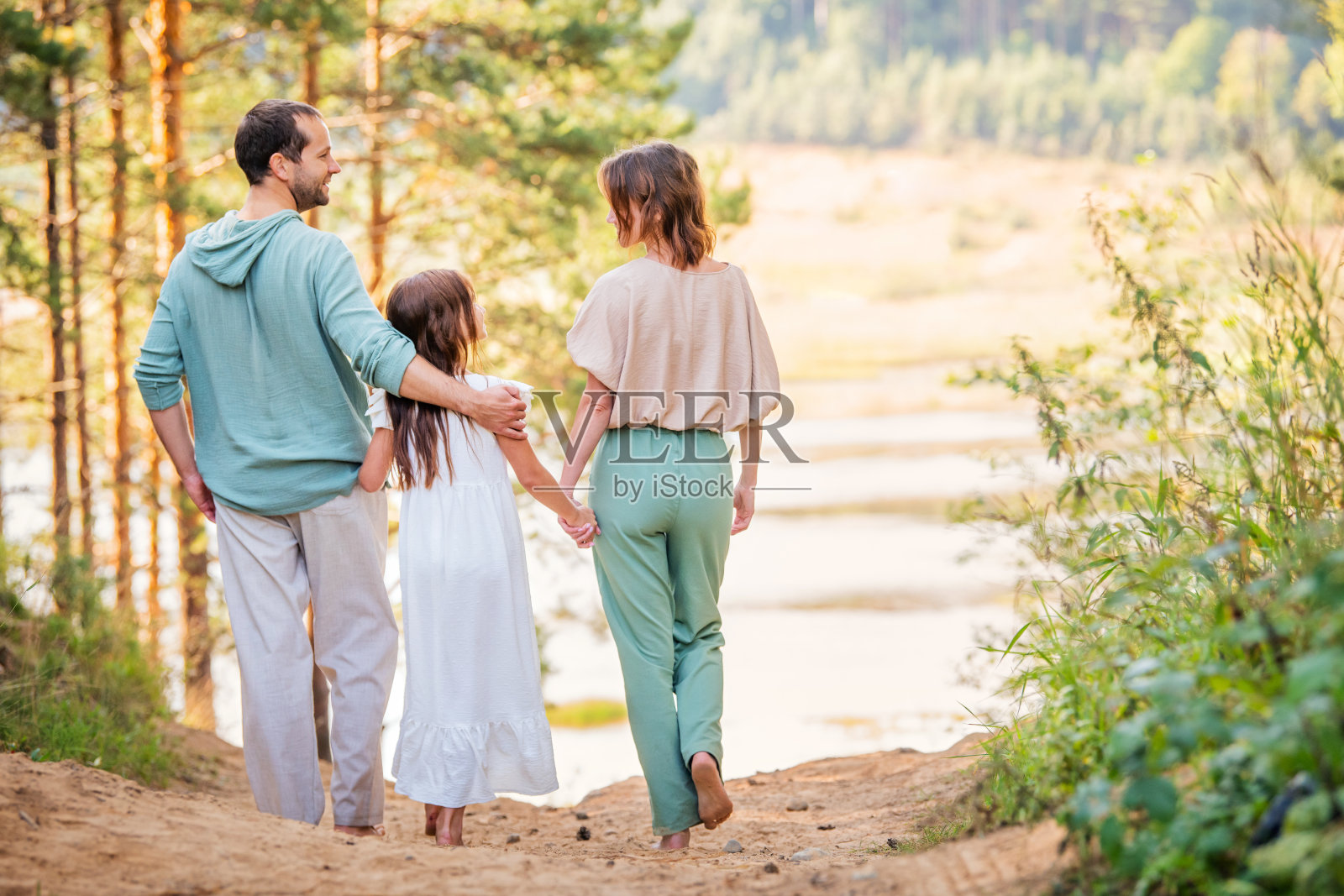 妈妈、爸爸和孩子在大自然中快乐地散步。幸福家庭概念。父母拉着孩子的手。照片摄影图片